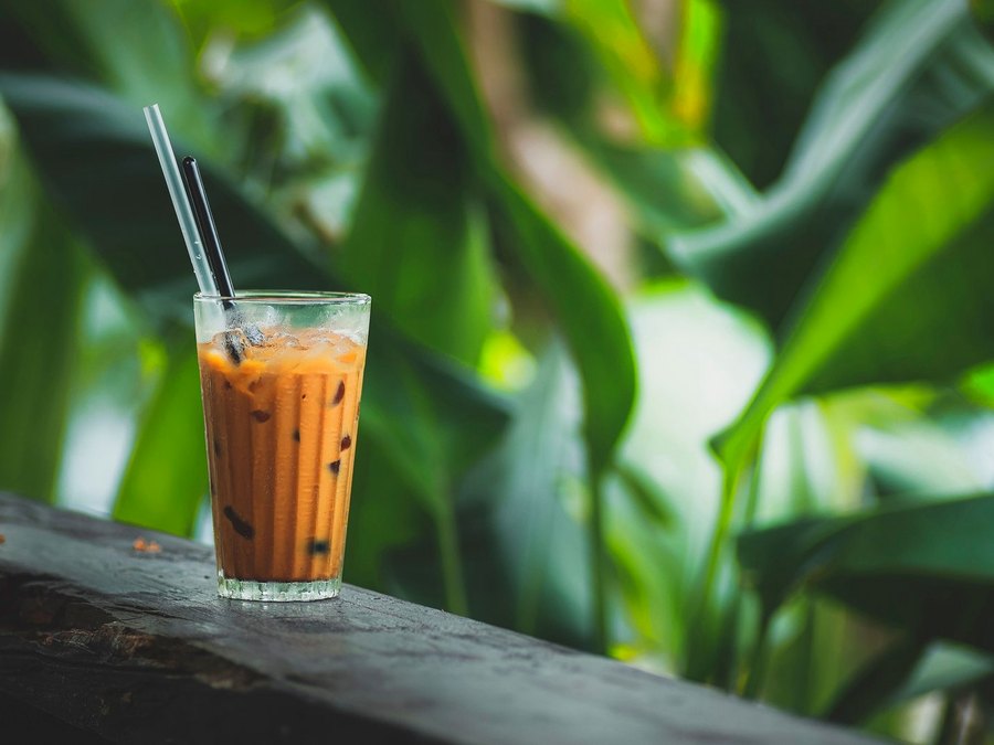 A tall glass of Thai milk tea against green leaves, illustrating ChaEn’s leaf-first approach
